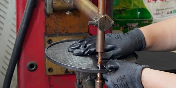 An employee performing spot welding on woven mesh