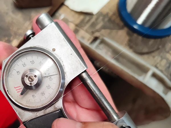 A person uses a micrometer to measure the stainless steel wire diameter.