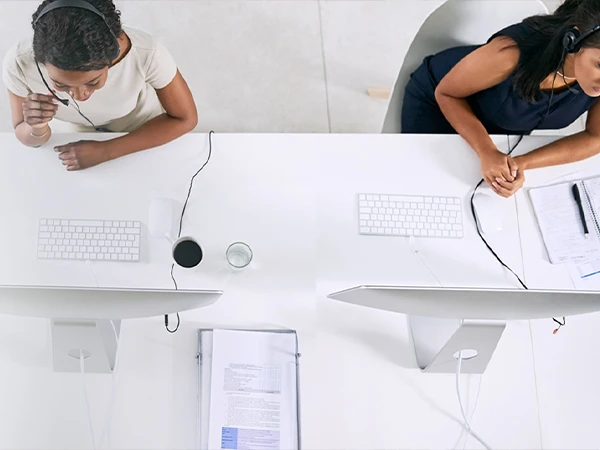 Two customer service representatives wearing headsets are responding to inquiries in front of computers.