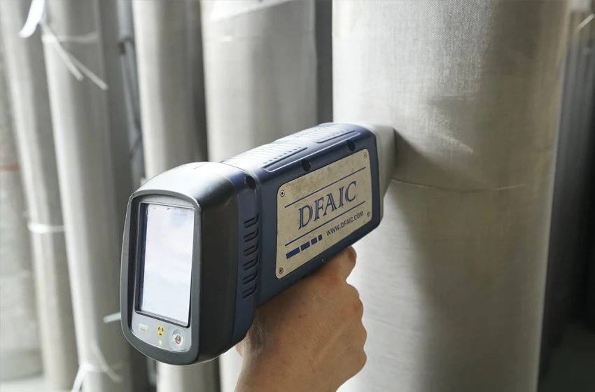 A hand is holding a tester for woven mesh chemical composition inspection.